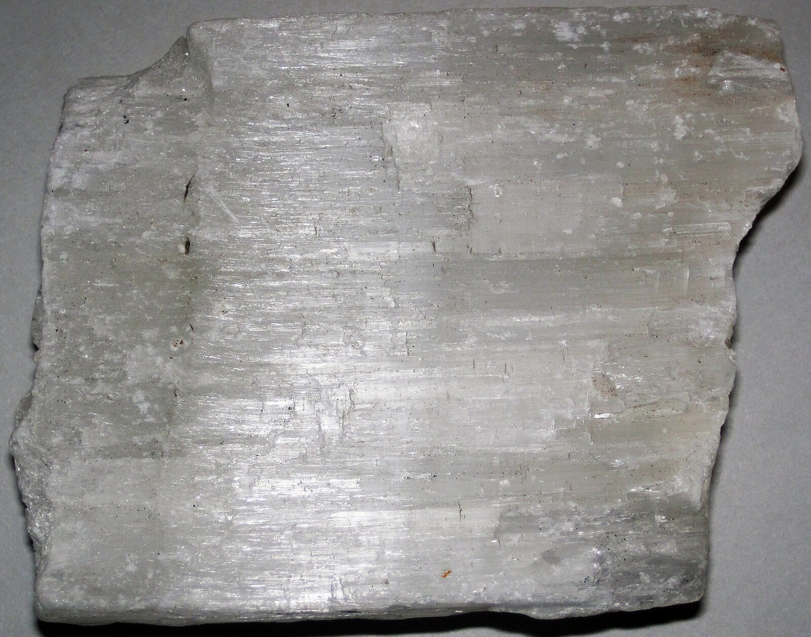 White satin spar gypsum with dense parallel fibers carrying bands of reflected light.